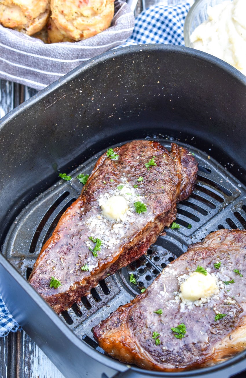 two garlic butter topped cooked steaks in the basket of an air fryer
