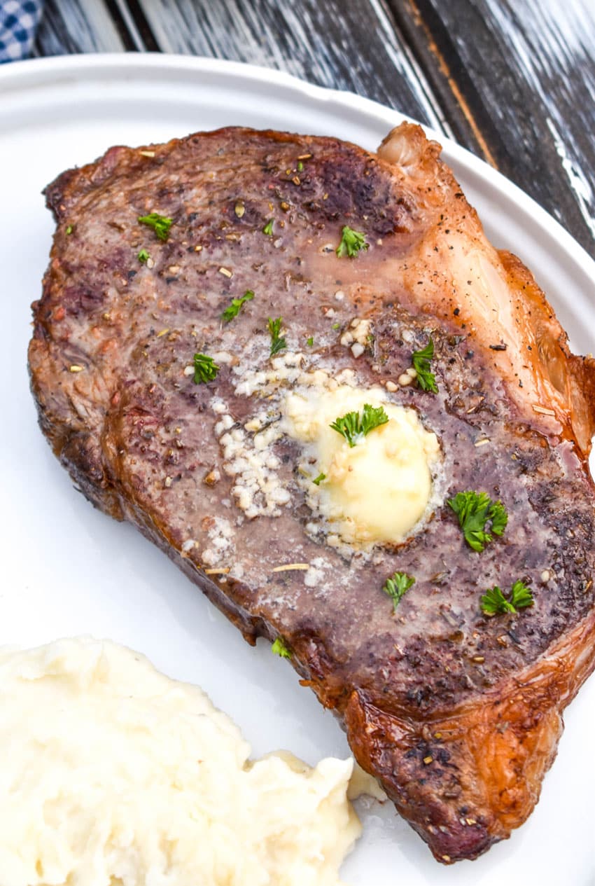 an air fried ribeye steak topped with garlic butter on a white dinner plate