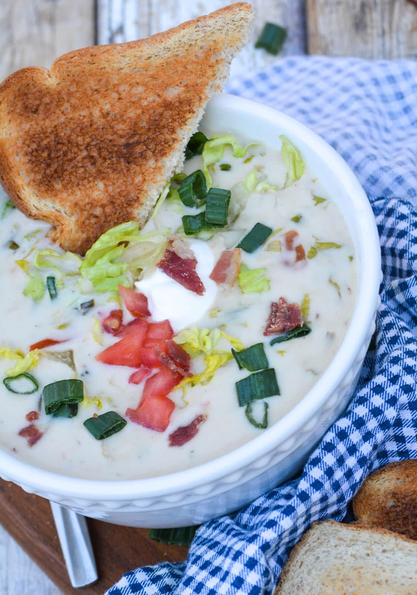 blt soup in a white bowl topped with lettuce tomato and bacon with a slice of toast on the side