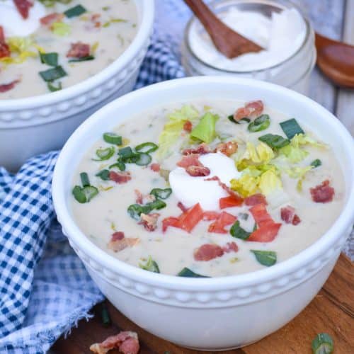 two white bowls filled with blt soup on a wooden cutting board
