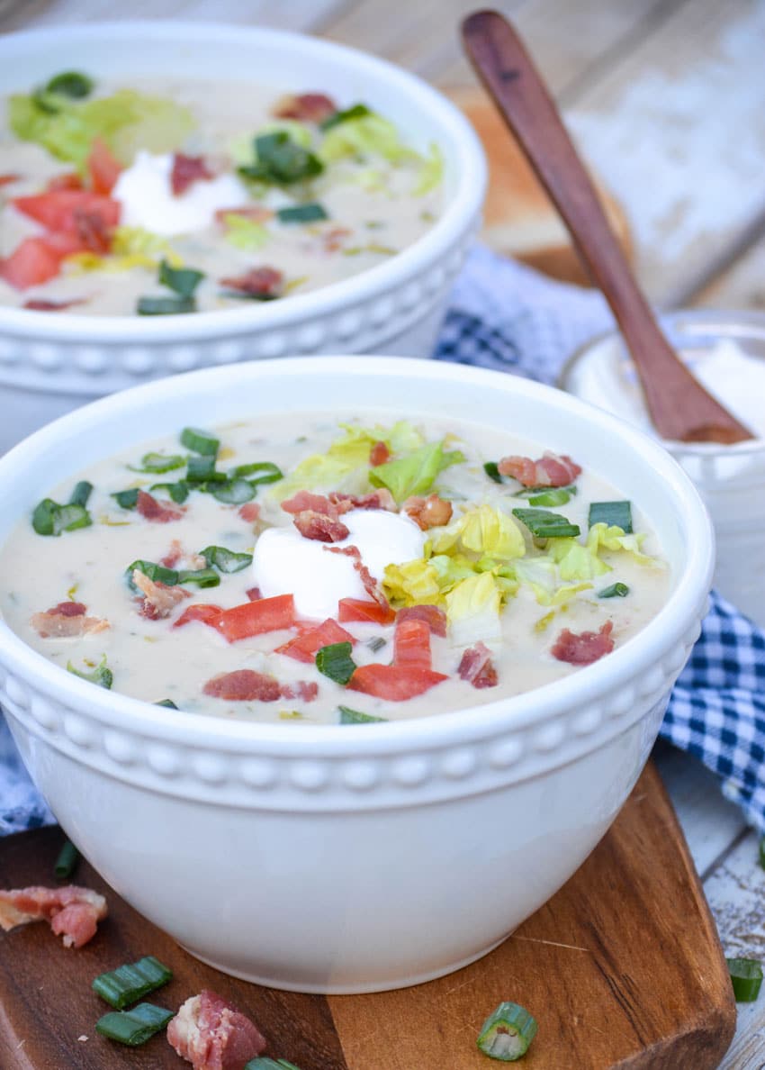 two white bowls filled with blt soup on a wooden cutting board