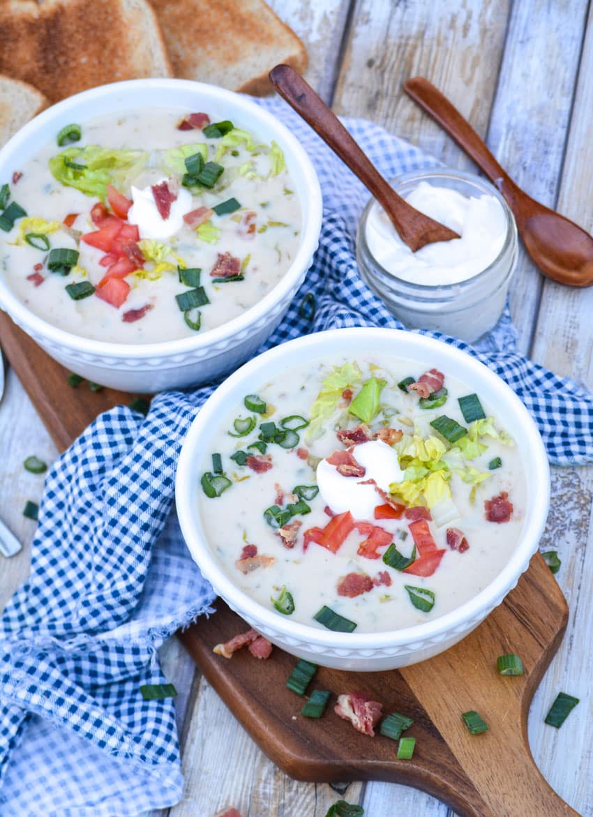 two white bowls filled with blt soup on a wooden cutting board
