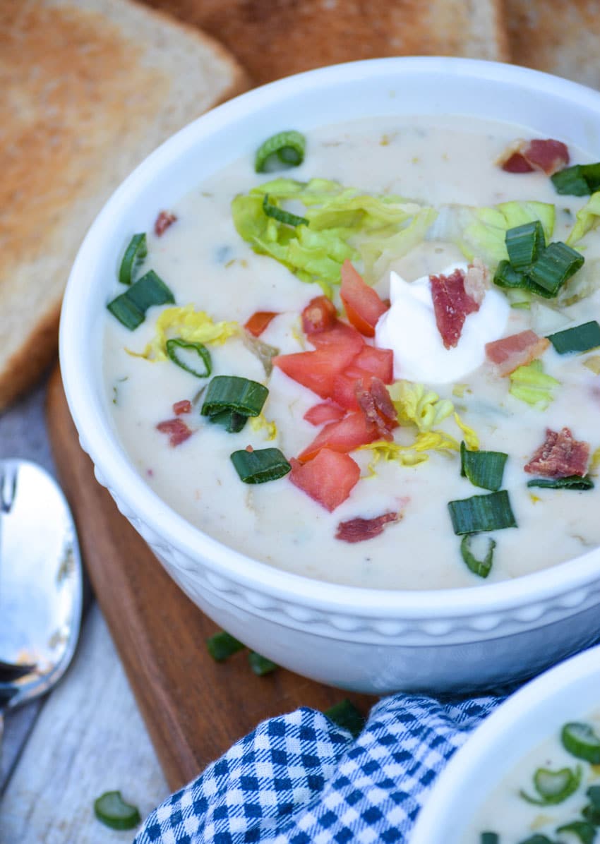 blt soup in a white bowl topped with lettuce tomato and bacon with a slice of toast on the side