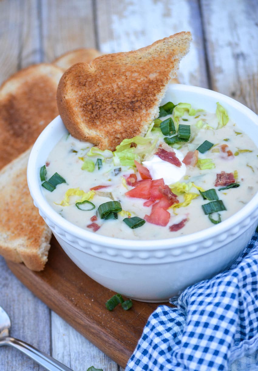 blt soup in a white bowl topped with lettuce tomato and bacon with a slice of toast on the side