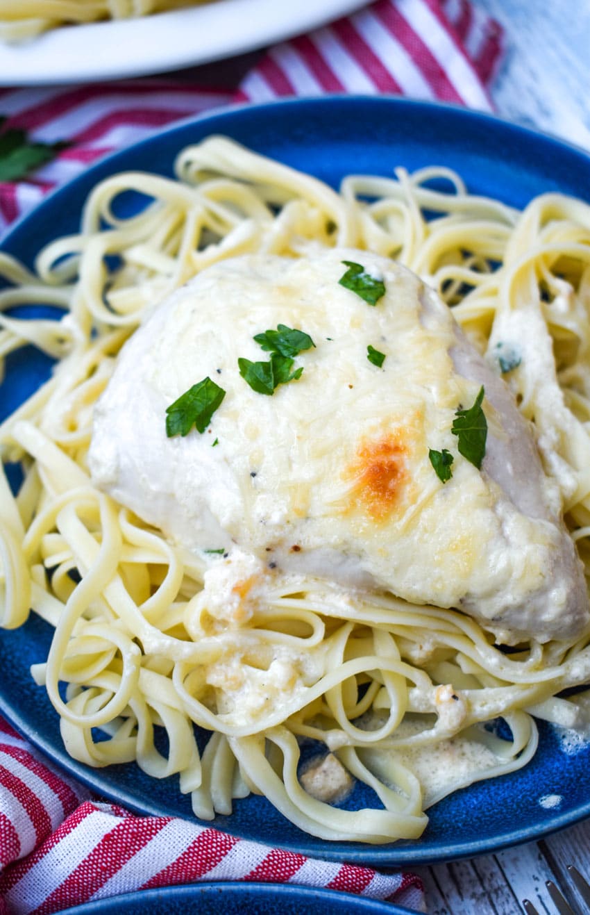 creamy caesar chicken over cooked pasta on blue plates