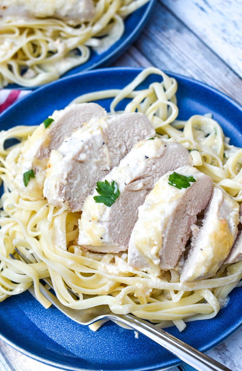 creamy caesar chicken over cooked pasta on blue plates