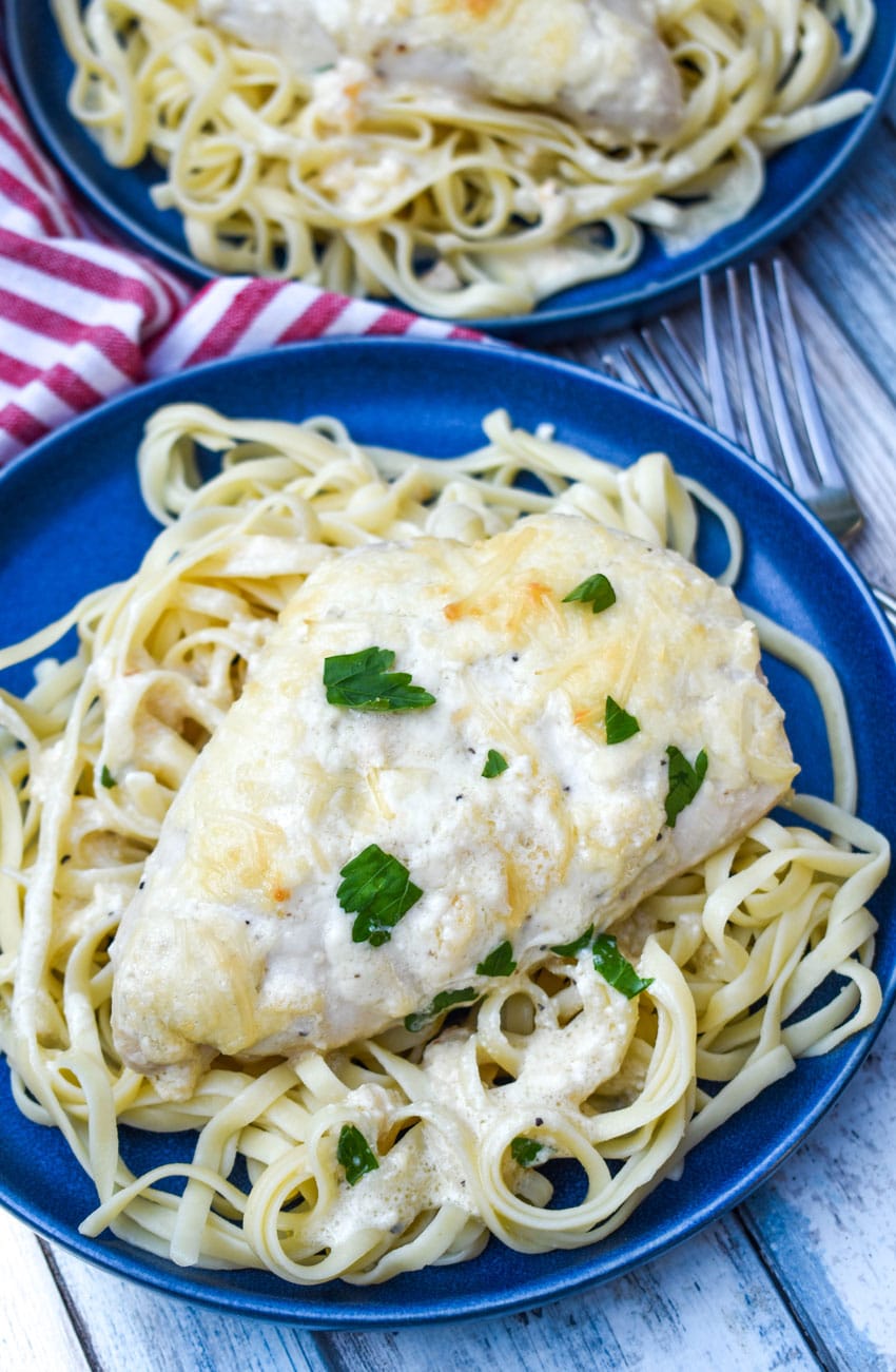 creamy caesar chicken over cooked pasta on blue plates