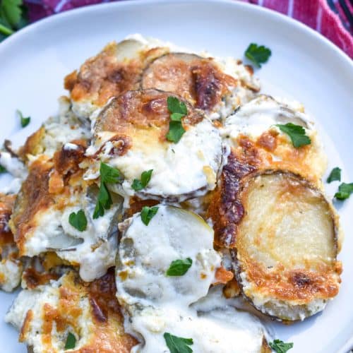 creamy scalloped potatoes with boursin cheese on a small white plate with a red cloth napkin on the side