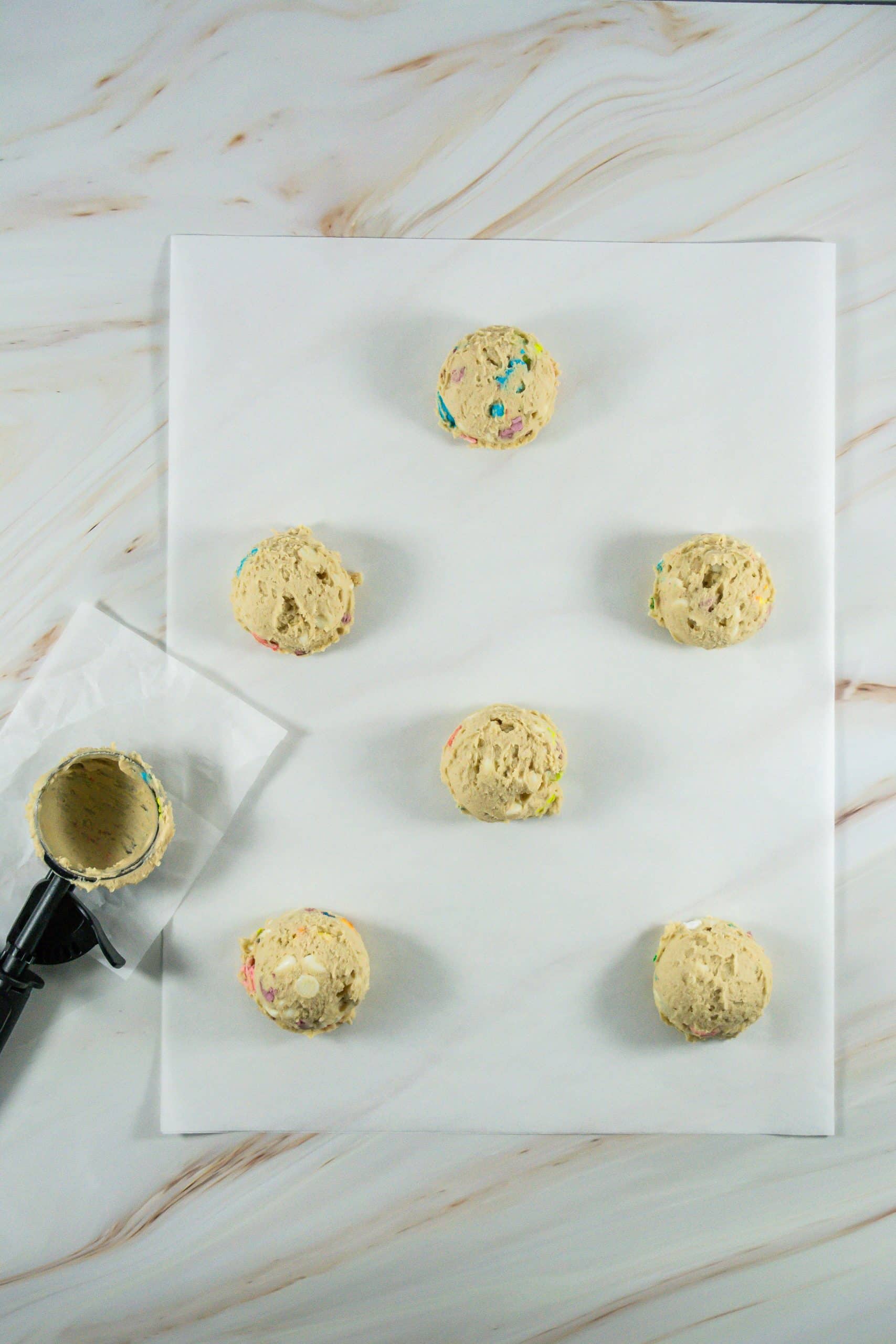 scoops of lucky charms cookie dough on a sheet of white parchment paper
