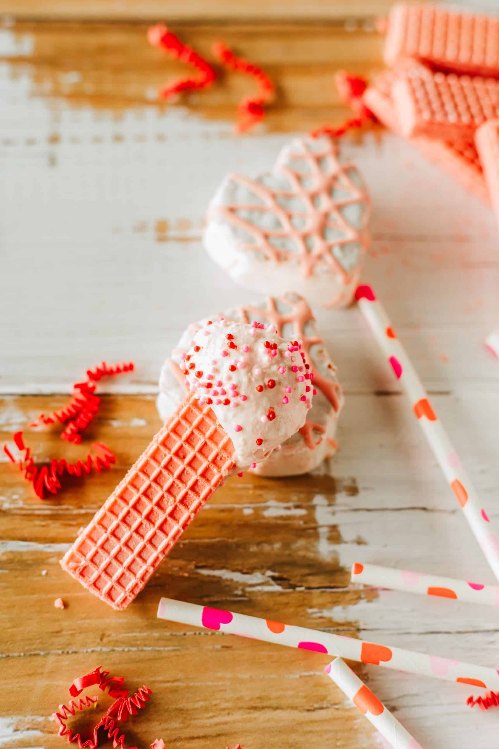 a pink wafer cookie topped with little debbie valentine cake dip resting on a wooden table