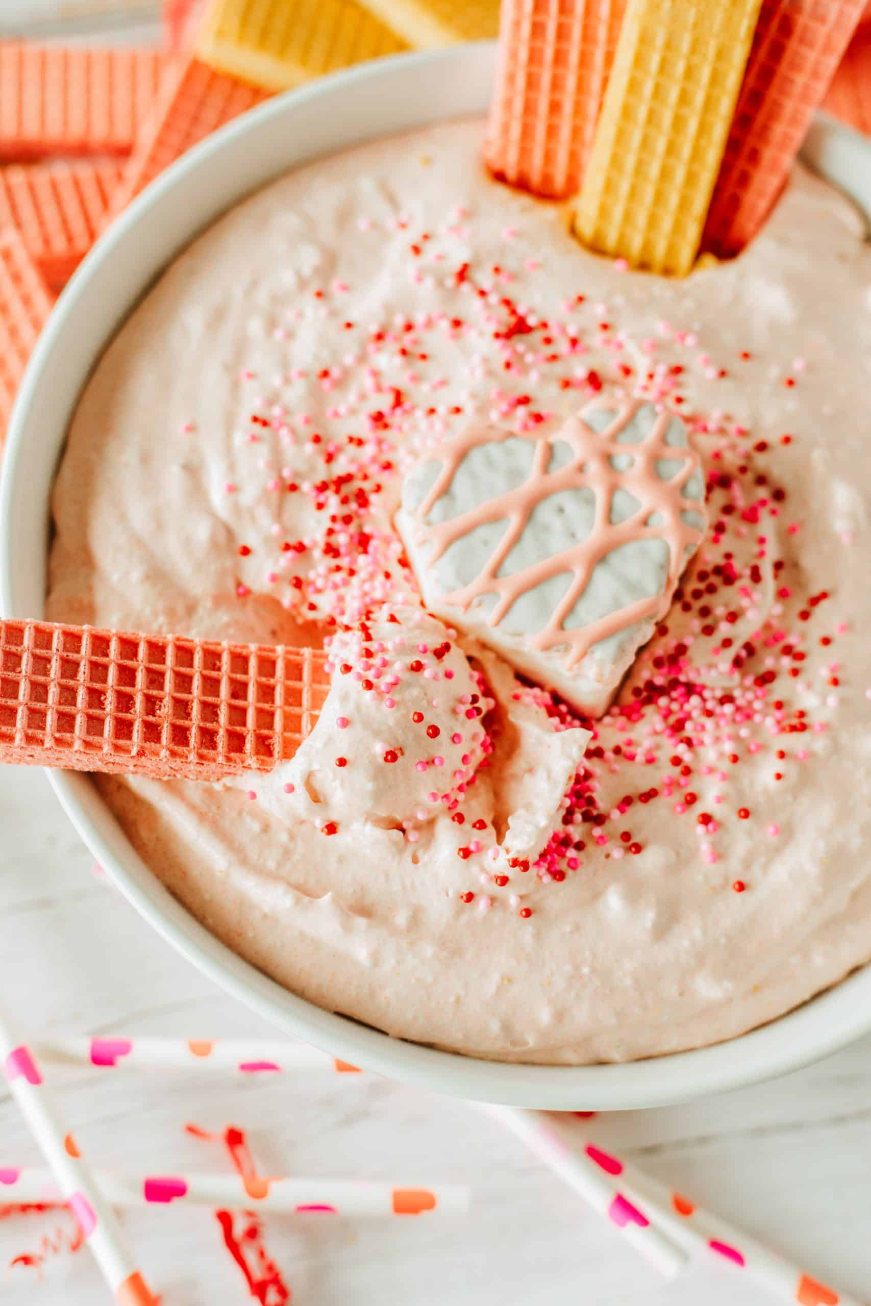 a vanilla wafer cookie stick in a bowl of Little Debbie Valentine cake dip in a white bowl topped with sprinkles and a snack cake