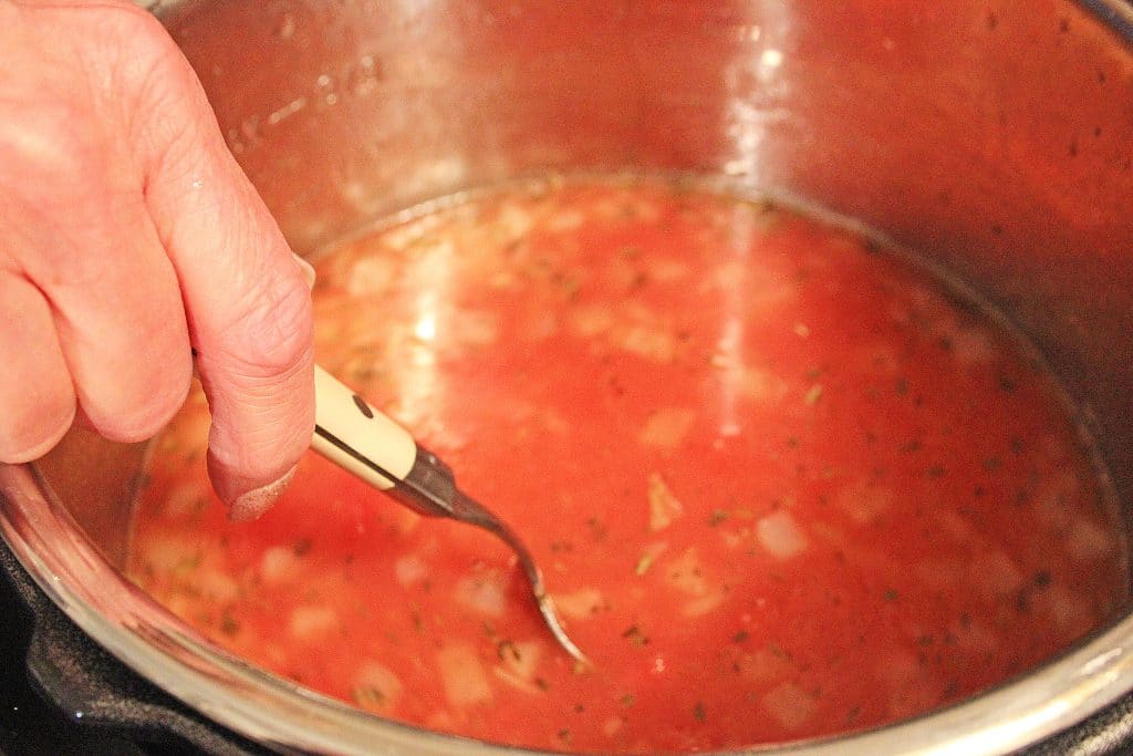 a spoon stirring tomato soup in the bowl of an instant pot
