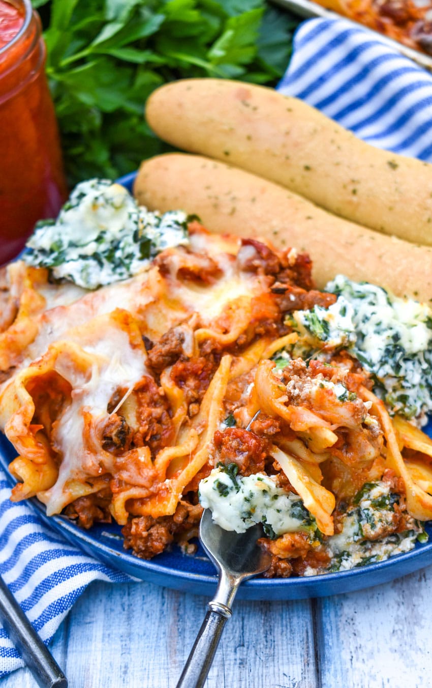 a silver fork resting on the edge of a blue plate topped with sheet pan lasagna with two breadsticks on the side
