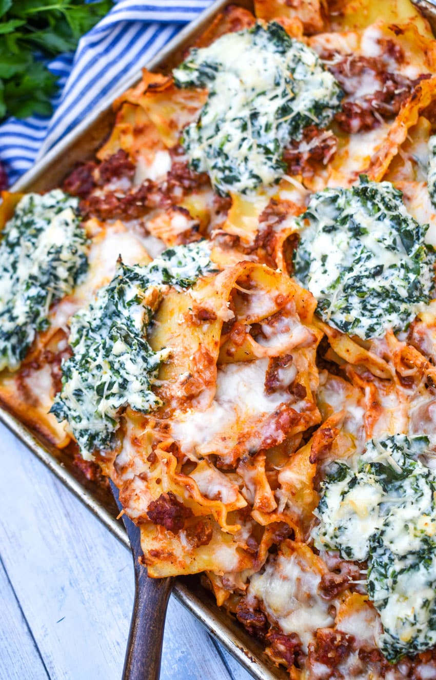 a wooden spatula scooping sheet pan lasagna off of a metal baking sheet