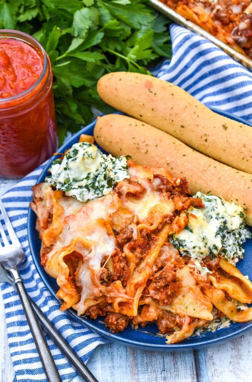 sheet pan lasagna shown on a blue plate with two breadsticks on the side