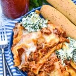 sheet pan lasagna shown on a blue plate with two breadsticks on the side