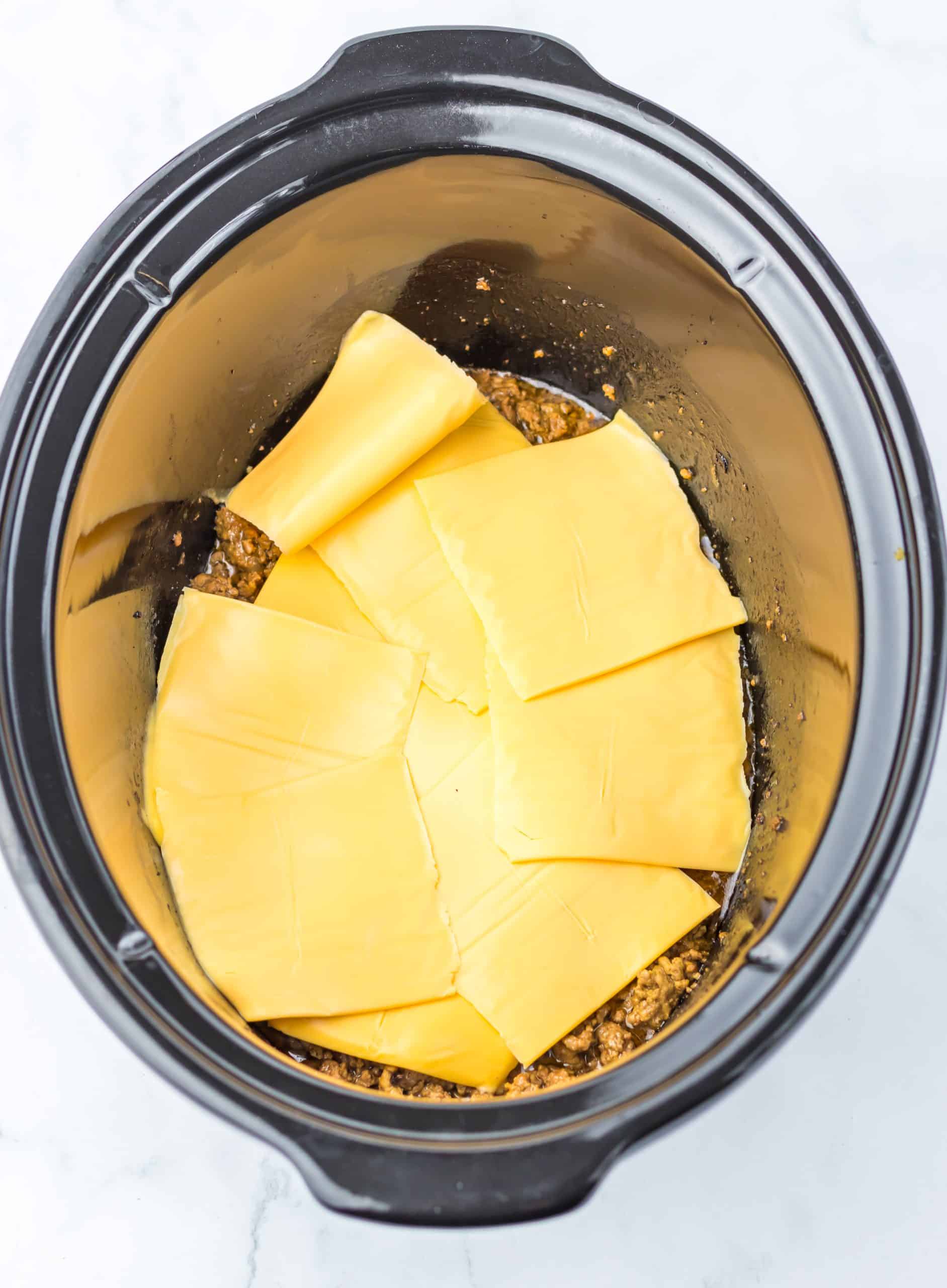 slices of American cheese over ground beef in the bowl of a slow cooker