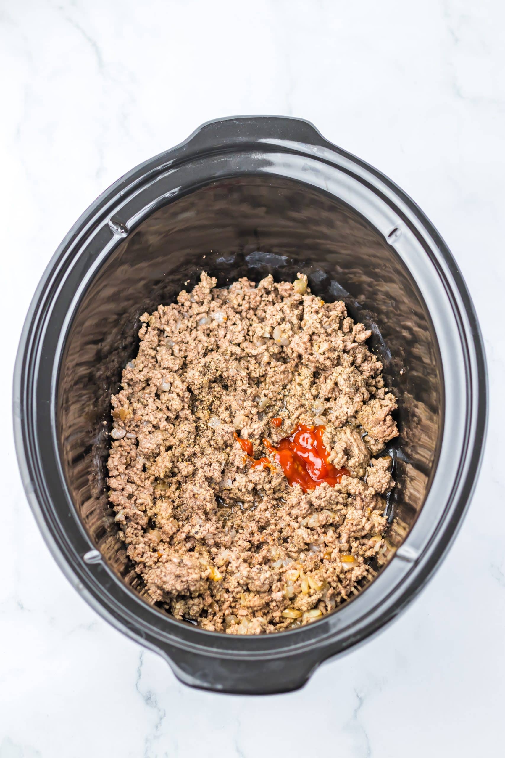 cooked ground beef and ketchup in the bowl of a slow cooker
