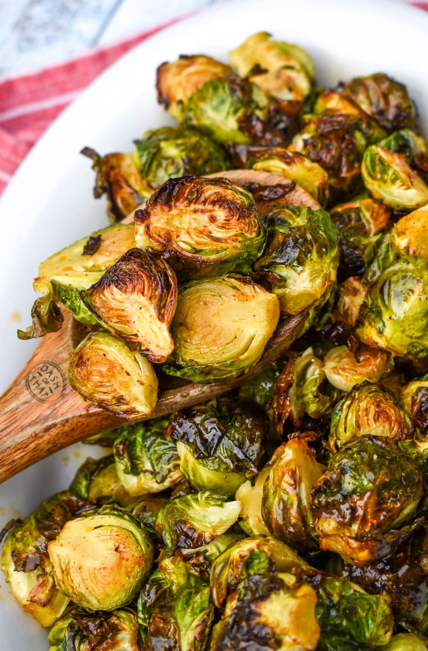 a wooden spoon scooping air fried brussels sprouts out of a white serving dish
