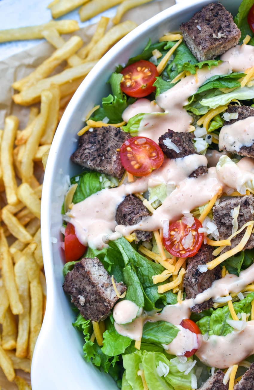 big mac salad with thousand island dressing in a large white serving bowl with french fries on the side