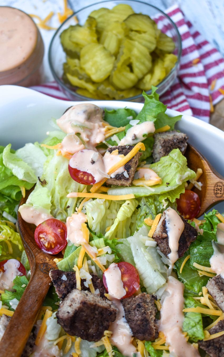 wooden salad servers digging into a bowl of cheeseburger salad