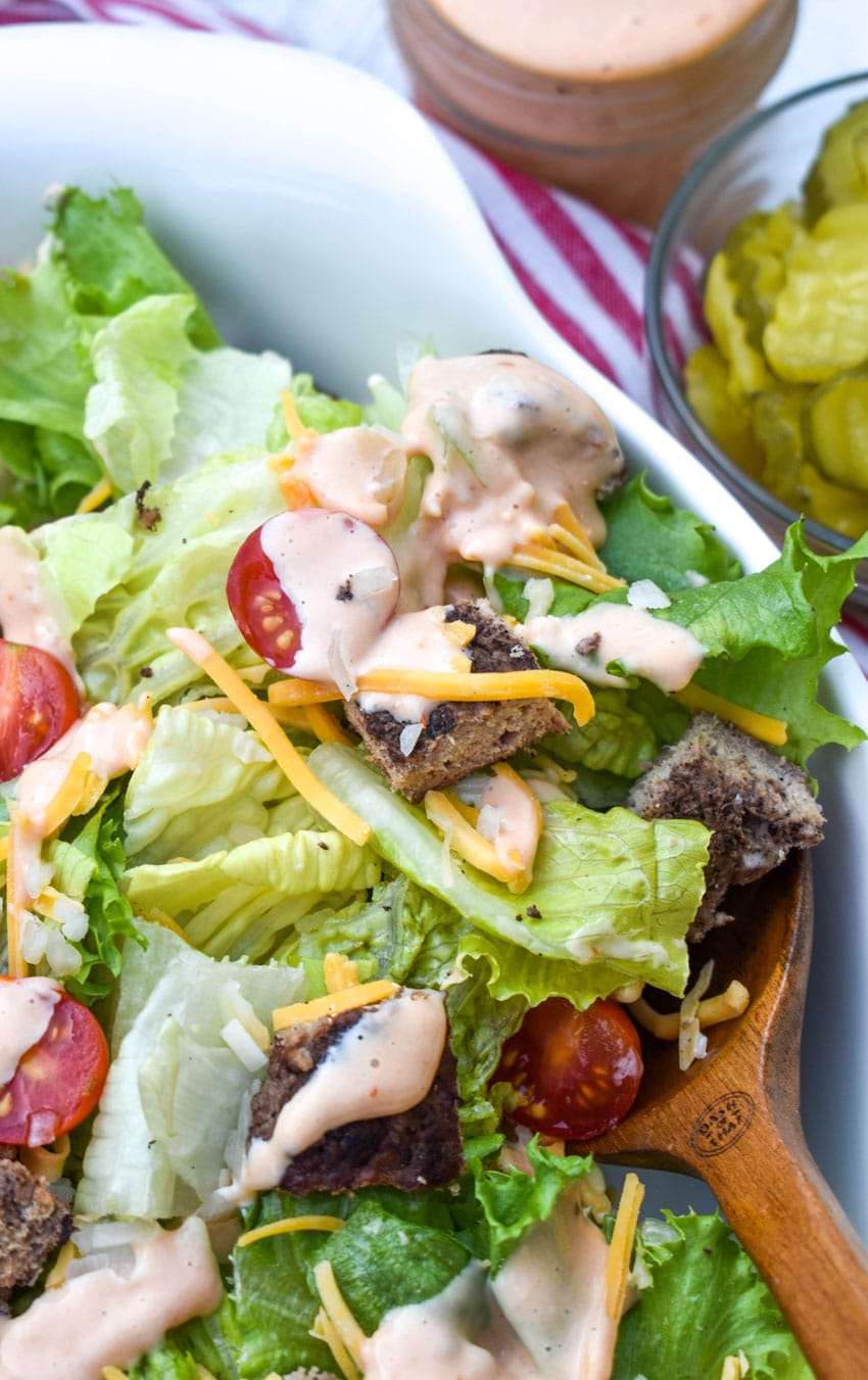 a wooden spoon scooping cheeseburger salad out of a large white bowl
