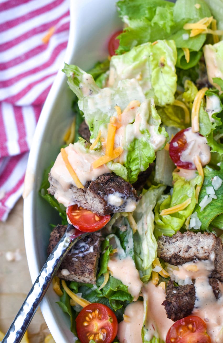 a silver fork resting on the edge of a white serving bowl filled with cheeseburger salad tossed with thousand island dressing