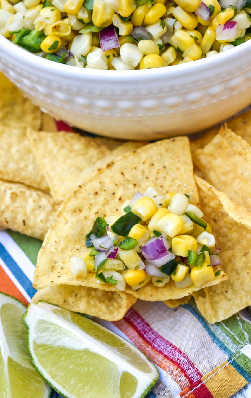 a corn tortilla topped with chipotle copycat corn salsa resting on other tortilla chips next to a white bowl