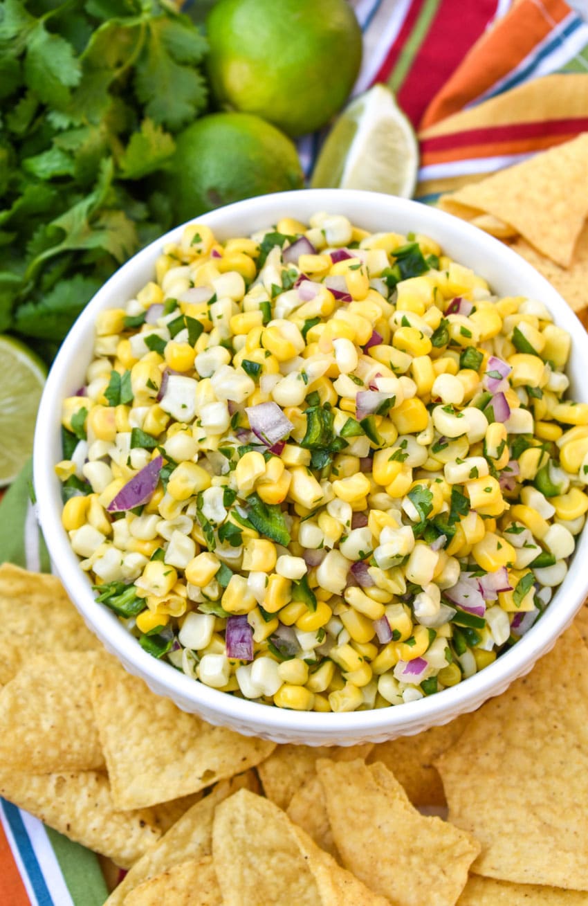 a homemade corn salsa recipe in a white bowl surrounded by tortilla chips