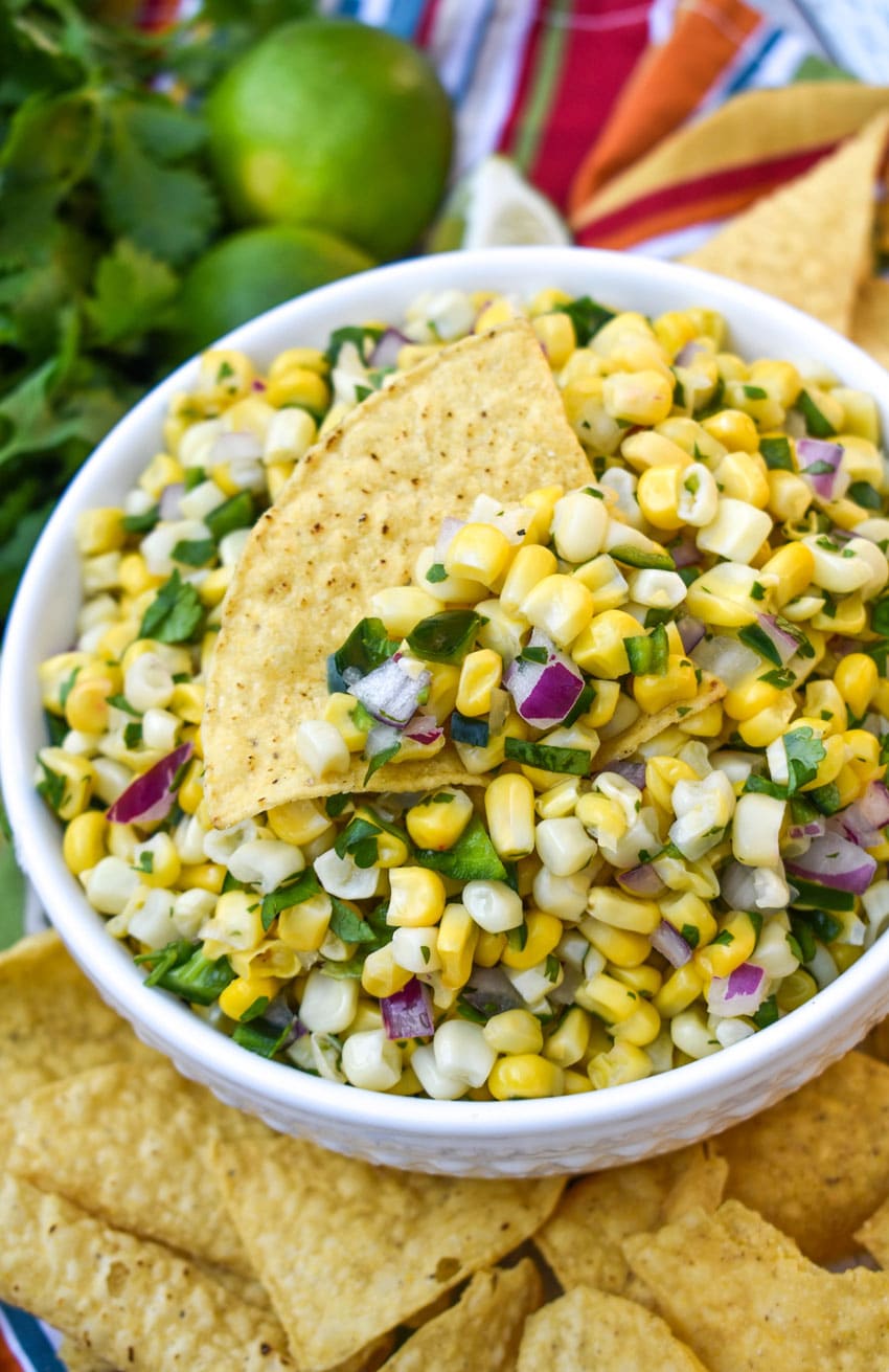 a tortilla chip scooping chipotle copycat corn salsa out of a white bowl