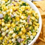a homemade corn salsa recipe in a white bowl surrounded by tortilla chips