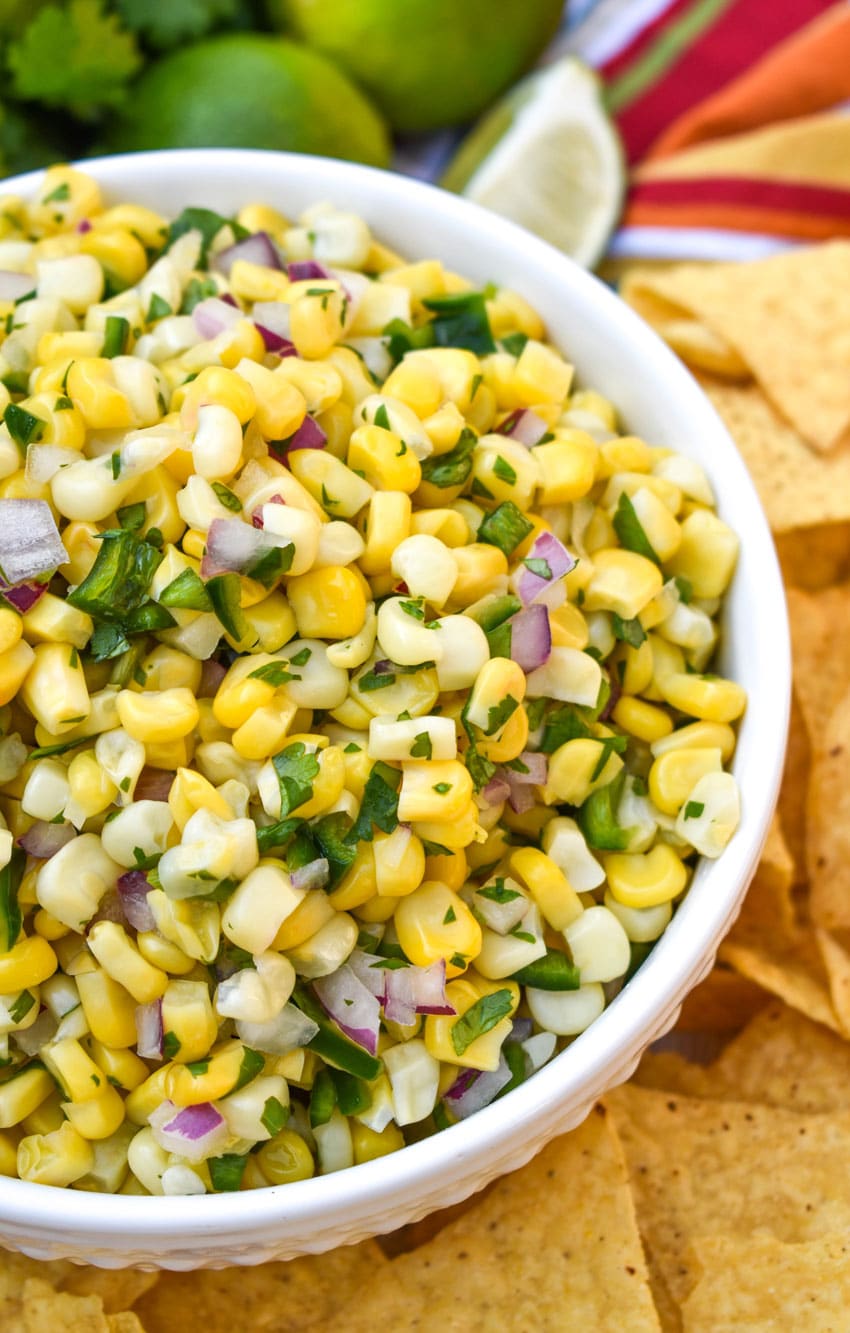 a homemade corn salsa recipe in a white bowl surrounded by tortilla chips