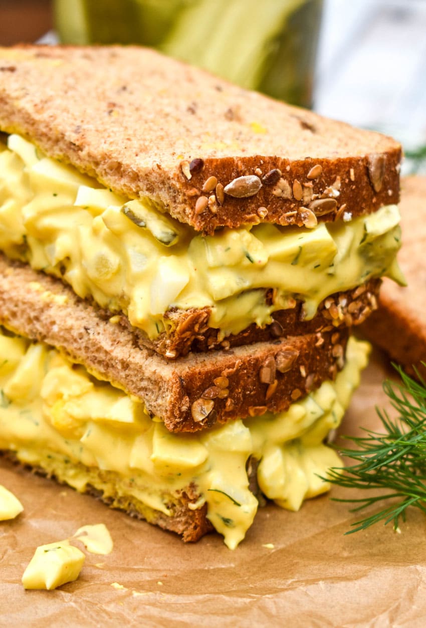 two halves of a dill pickle egg salad sandwich stacked on brown parchment paper