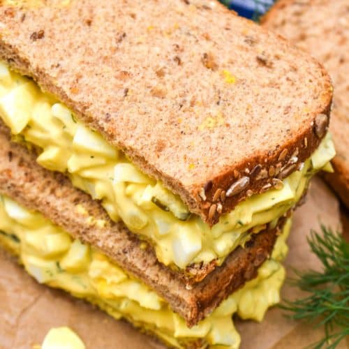 two halves of a dill pickle egg salad sandwich stacked on brown parchment paper
