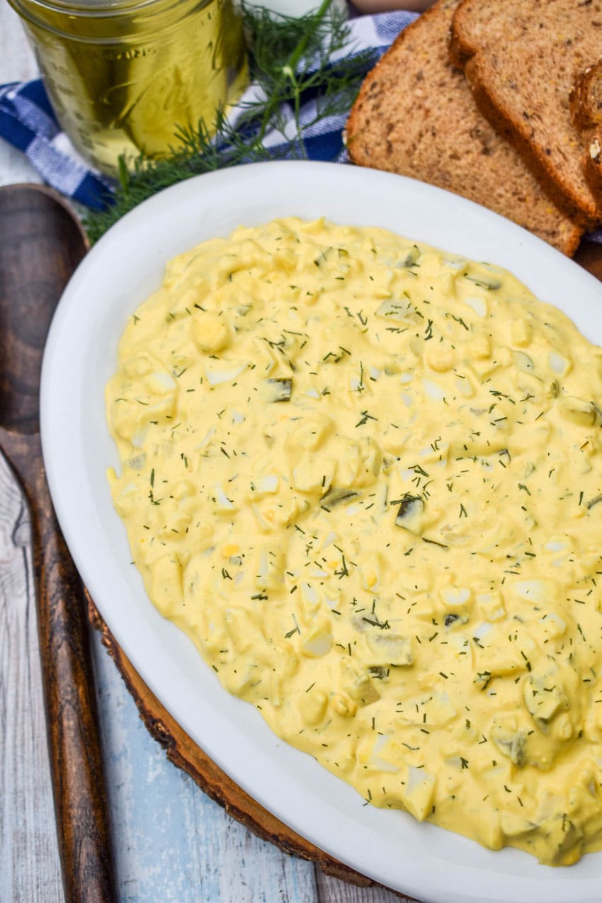 dill pickle egg salad in a large white serving bowl with a wooden spoon on the side