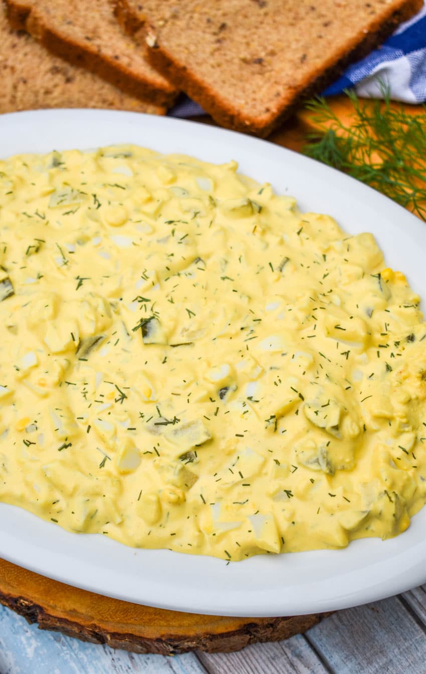 dill pickle egg salad in a large white serving bowl with a wooden spoon on the side