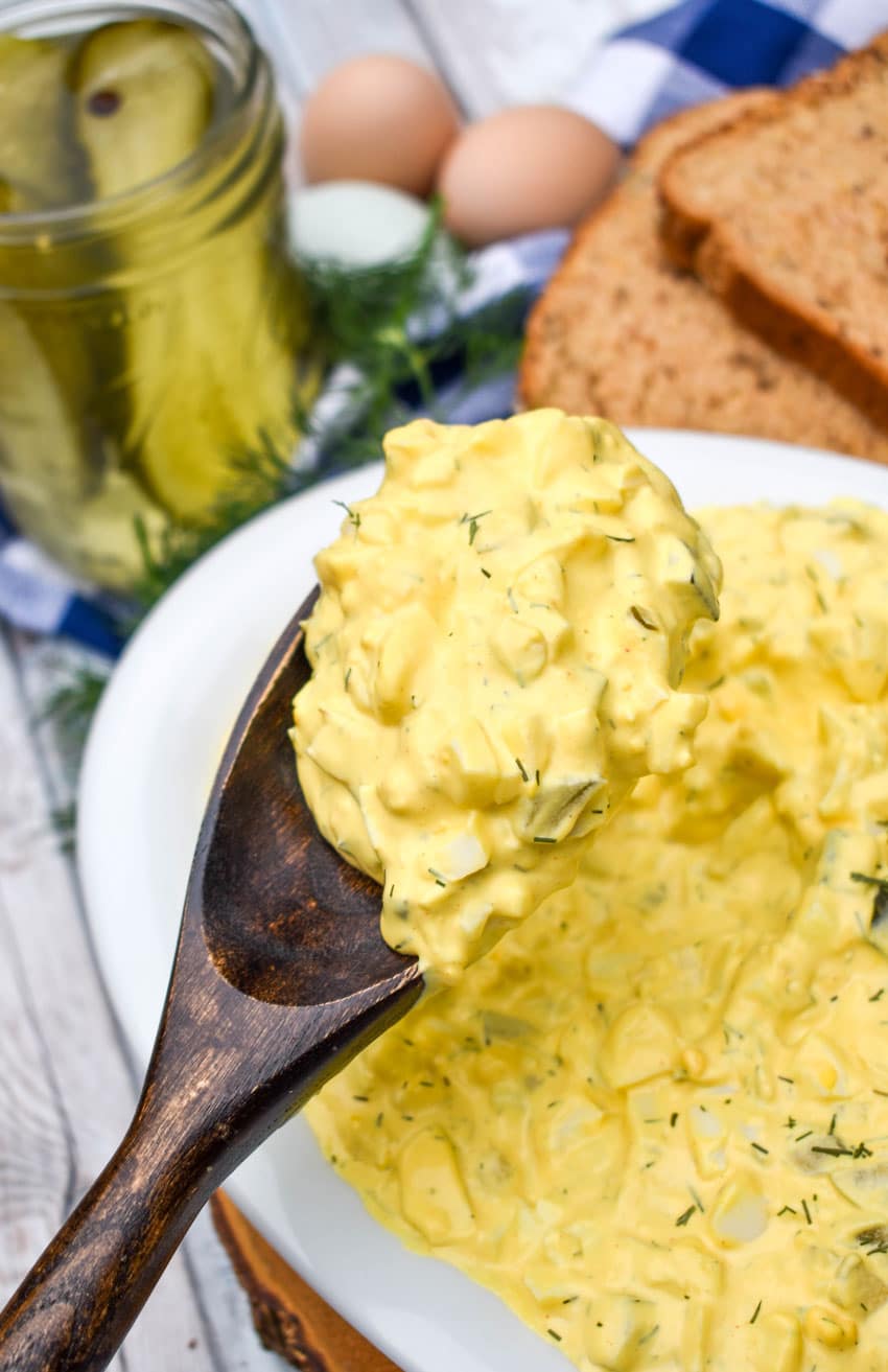 a wooden spoon holding up a scoop of dill pickle egg salad