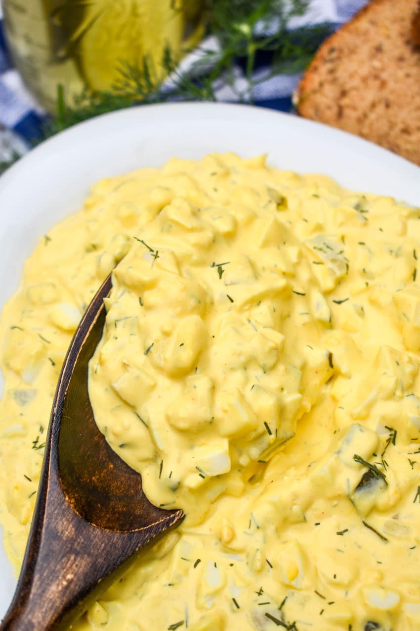 a wooden spoon scooping dill pickle egg salad out of a white serving bowl