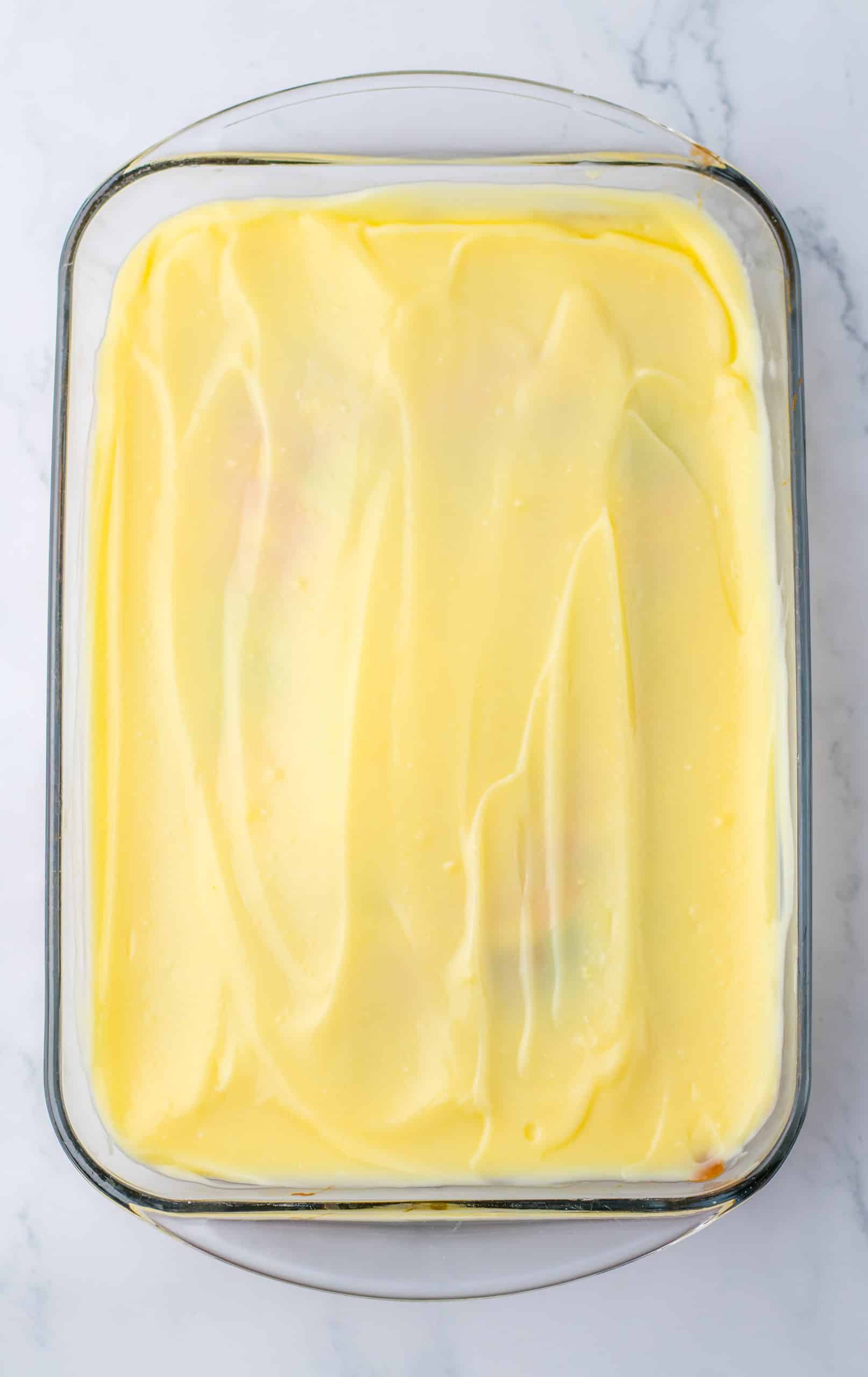 vanilla pudding spread overtop of a baked cake in a glass baking dish