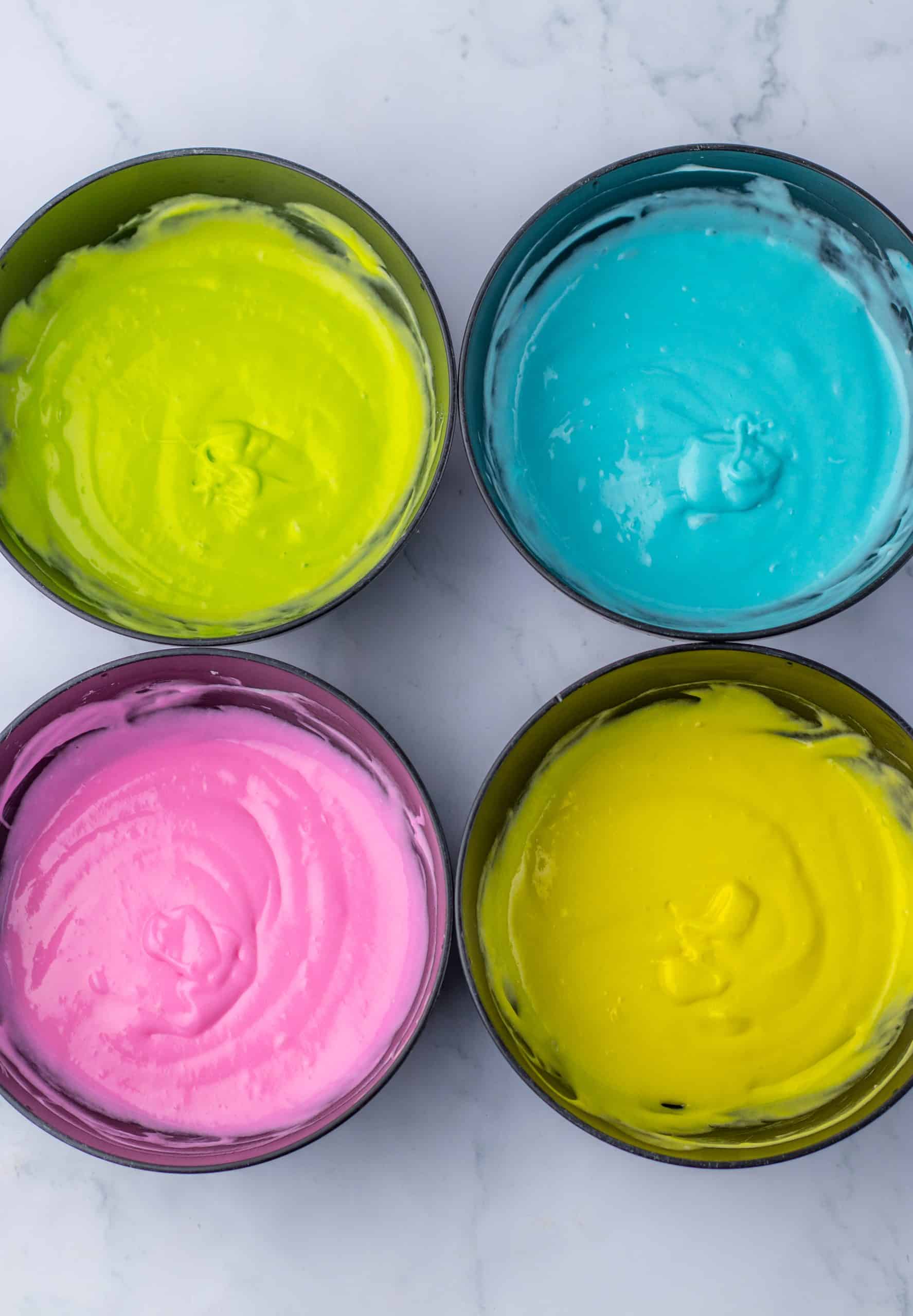 four cake pans filled with different pastel colors of cake batter