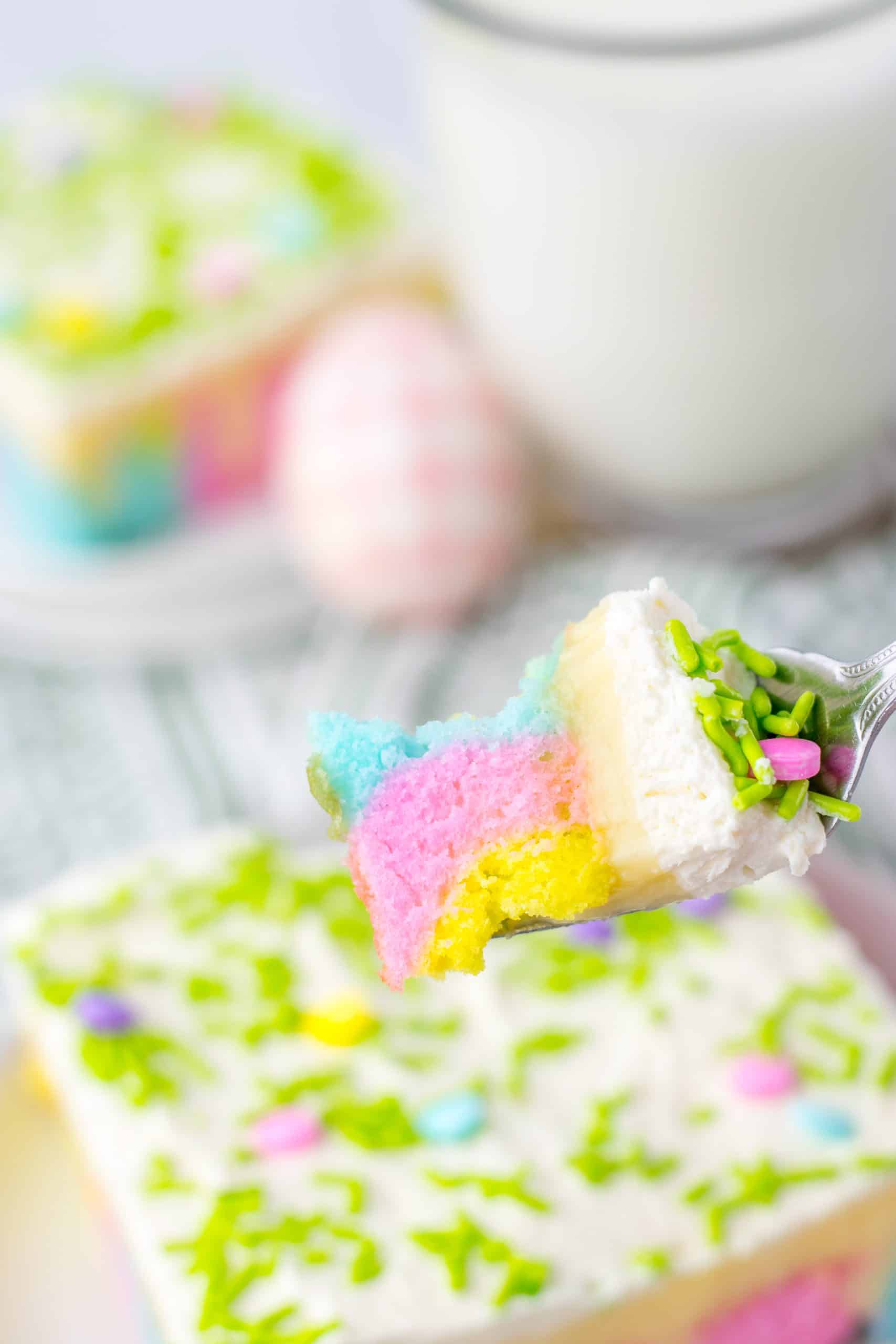 a silver fork holding up a scoop of a pastel colored sprinkle topped easter poke cake
