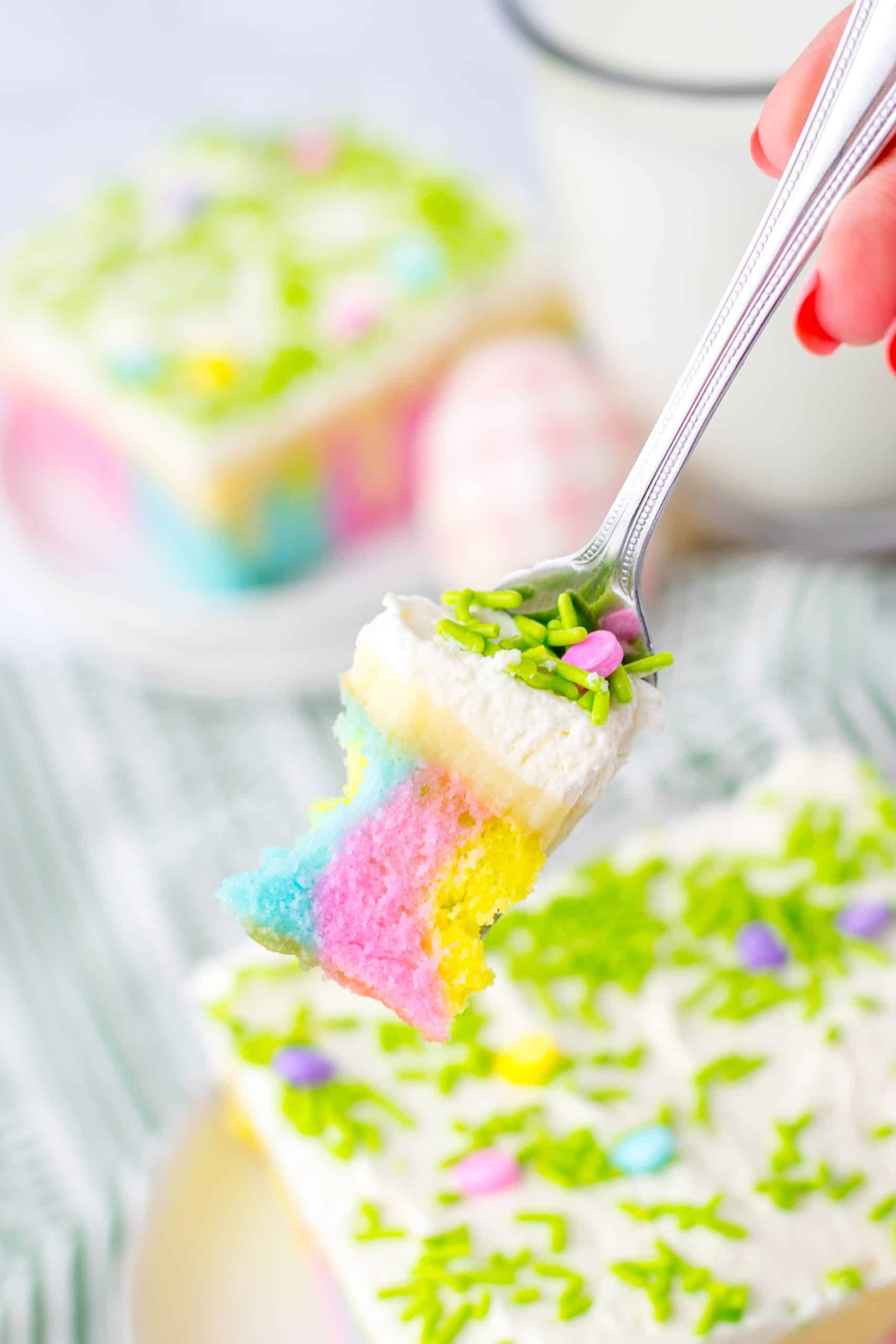 a silver fork holding up a scoop of a pastel colored sprinkle topped easter poke cake