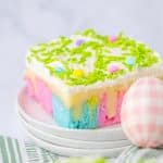 a slice of pastel rainbow colored easter poke cake on a small white dessert plate with a glass of milk in the background