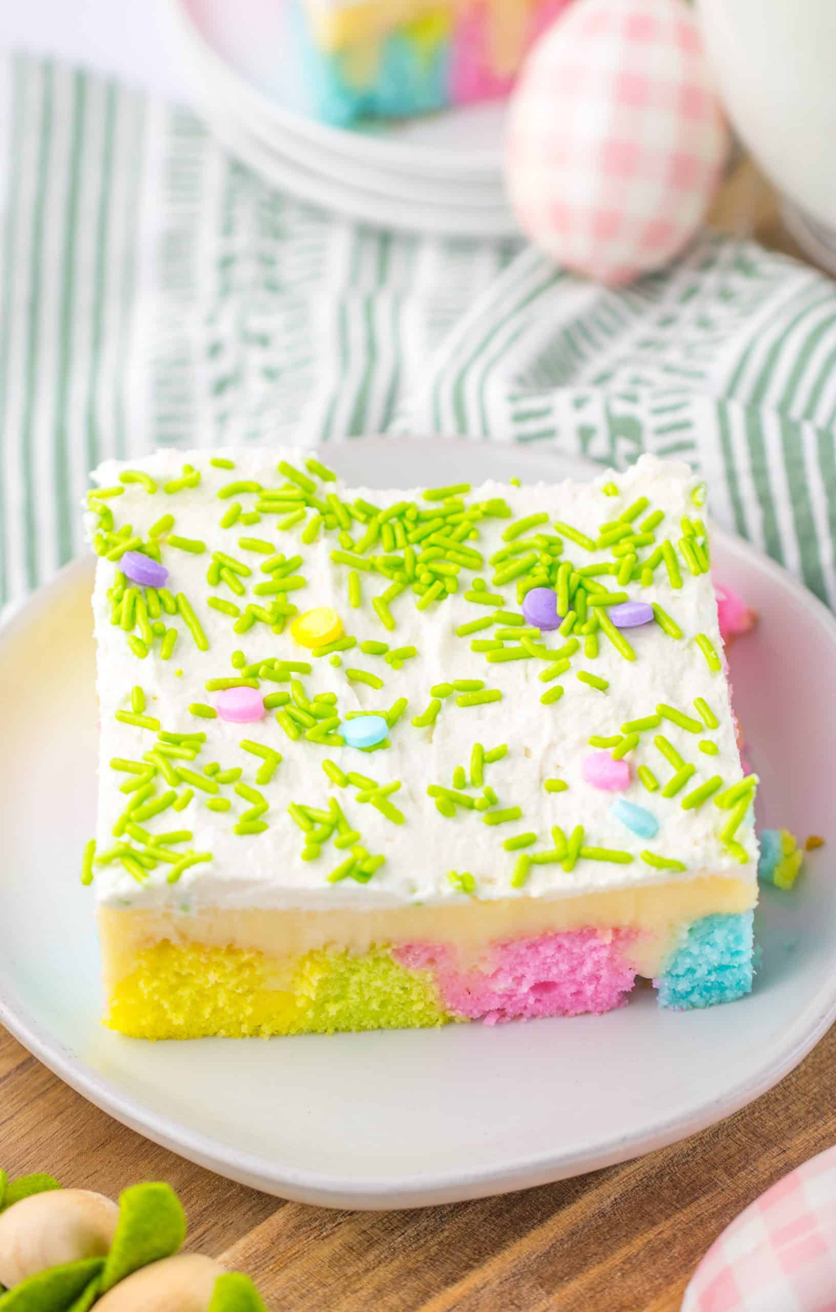 a slice of pastel rainbow colored easter poke cake on a small white dessert plate with a glass of milk in the background