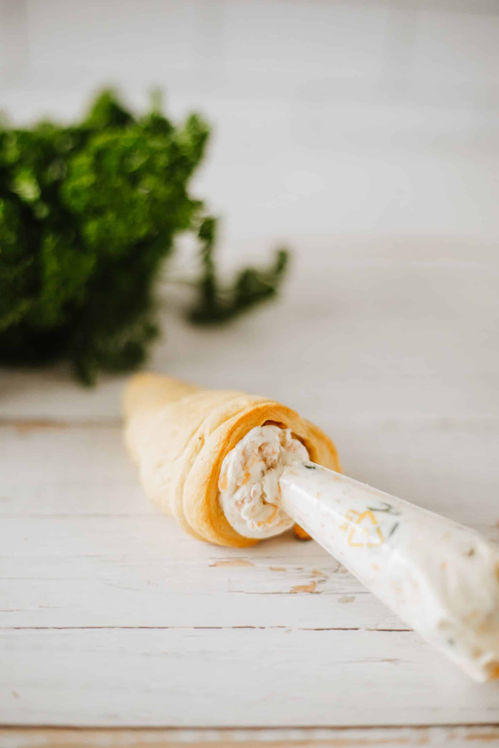 carrot crescent rolls with bacon cheddar cream cheese filling piped in resting on a wooden table with piping bag on the side