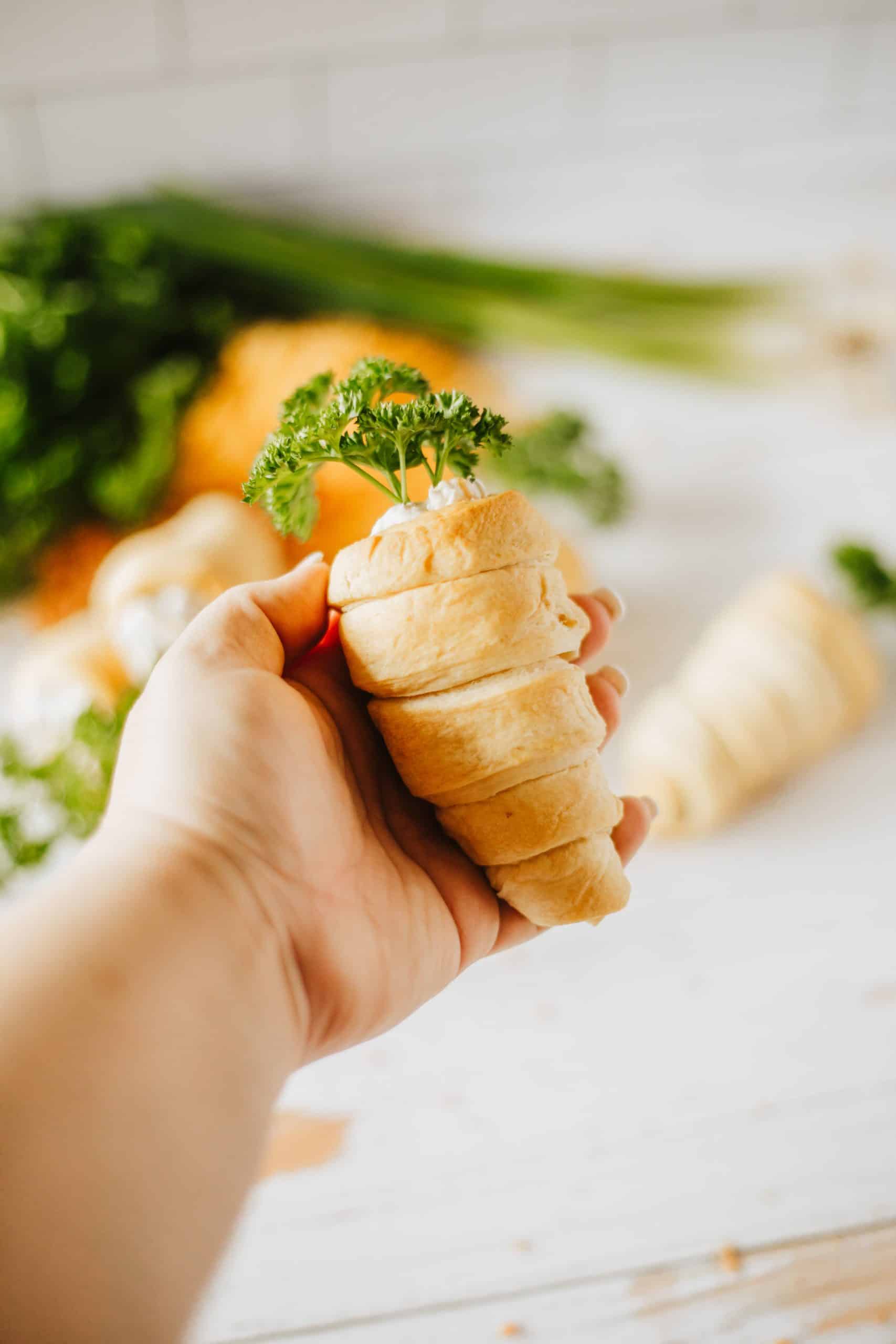 a hand holding up a bacon cheddar cream cheese stuffed carrot crescent rolls
