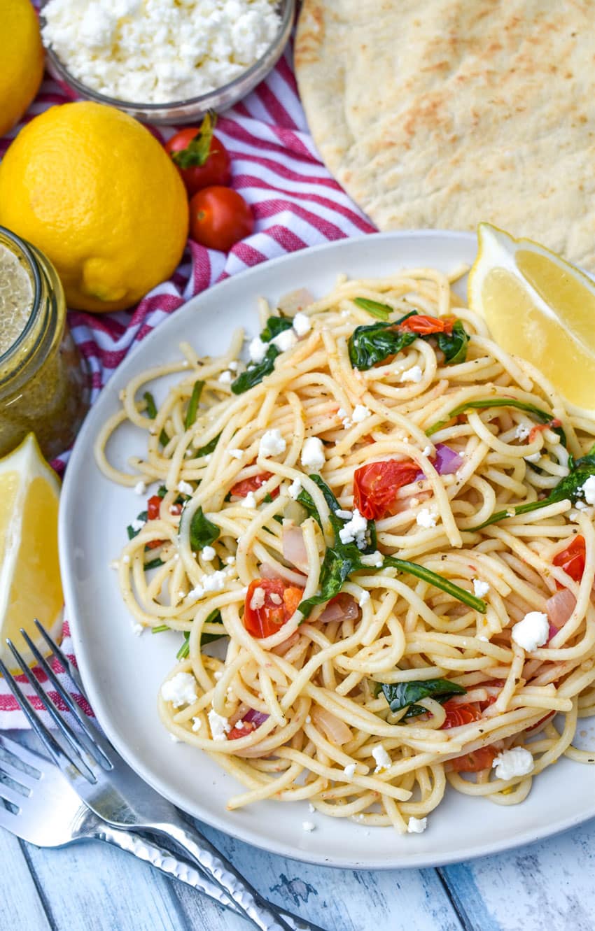 easy greek spaghetti on a gray plate with a fresh lemon wedge on the side