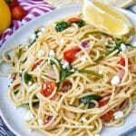 easy greek spaghetti on a gray plate with a fresh lemon wedge on the side