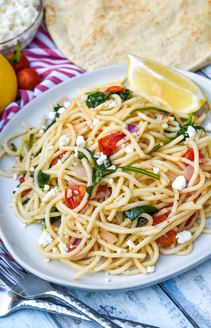easy greek spaghetti on a gray plate with a fresh lemon wedge on the side
