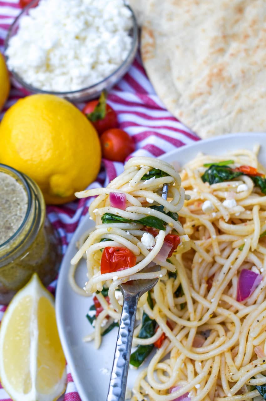 a silver fork lifting a scoop of greek spaghetti off a gray plate